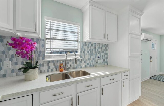 kitchen featuring light hardwood / wood-style flooring, sink, a wall mounted AC, decorative backsplash, and white cabinetry