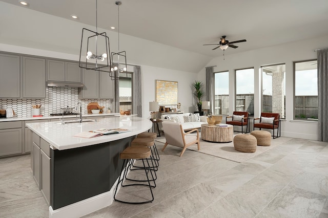 kitchen featuring ceiling fan with notable chandelier, sink, hanging light fixtures, lofted ceiling, and a center island with sink