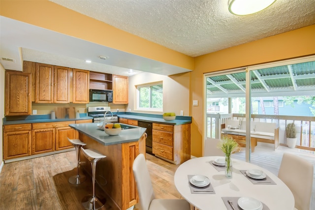 kitchen featuring light hardwood / wood-style flooring, black appliances, a kitchen island, a textured ceiling, and a kitchen breakfast bar