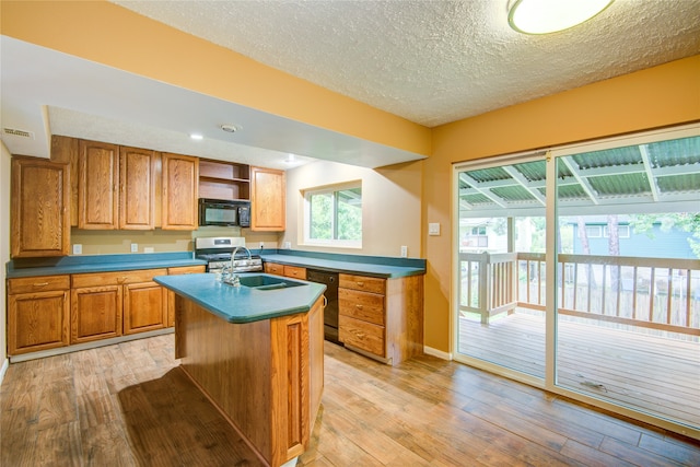 kitchen featuring light hardwood / wood-style flooring, a textured ceiling, a kitchen island with sink, black appliances, and sink