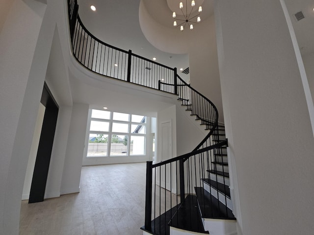 staircase with hardwood / wood-style floors, a towering ceiling, and an inviting chandelier