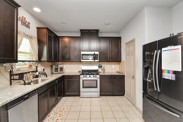 kitchen featuring light tile patterned floors, stainless steel appliances, light stone counters, and sink