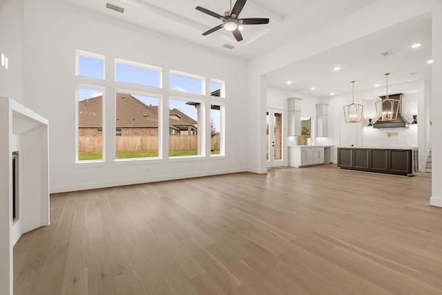 unfurnished living room with a high ceiling, ceiling fan with notable chandelier, sink, and light hardwood / wood-style flooring