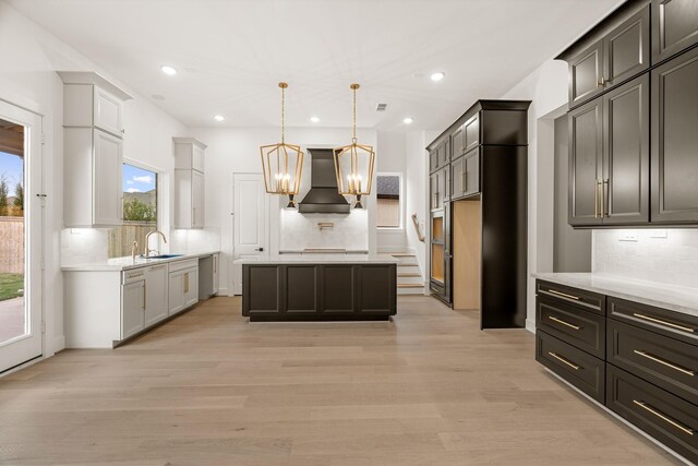 kitchen featuring a center island, custom range hood, pendant lighting, light hardwood / wood-style floors, and backsplash