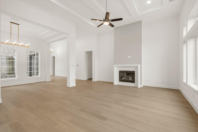 unfurnished living room with ceiling fan with notable chandelier, light hardwood / wood-style flooring, a towering ceiling, and beamed ceiling