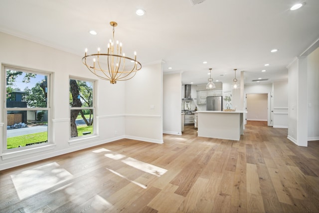 interior space with wall chimney range hood, light wood-type flooring, decorative light fixtures, a notable chandelier, and stainless steel refrigerator