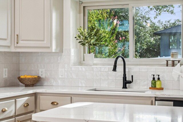 kitchen featuring backsplash, light stone countertops, white cabinetry, and a sink