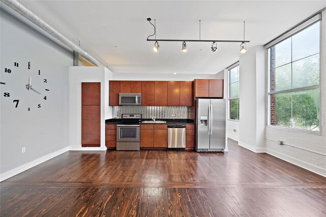 kitchen with appliances with stainless steel finishes, track lighting, backsplash, and dark hardwood / wood-style flooring