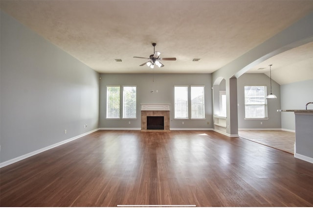 unfurnished living room with ceiling fan, a tiled fireplace, hardwood / wood-style floors, and lofted ceiling