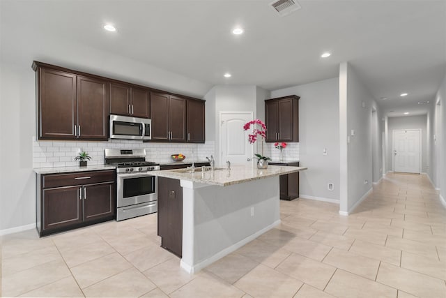 kitchen featuring light stone countertops, an island with sink, stainless steel appliances, sink, and light tile patterned flooring