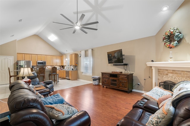 living room with light wood-type flooring, a fireplace, vaulted ceiling, and ceiling fan