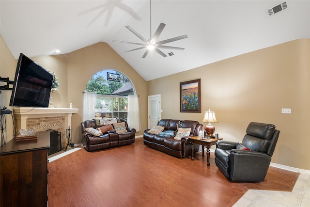 living room featuring a brick fireplace, light hardwood / wood-style flooring, high vaulted ceiling, and ceiling fan