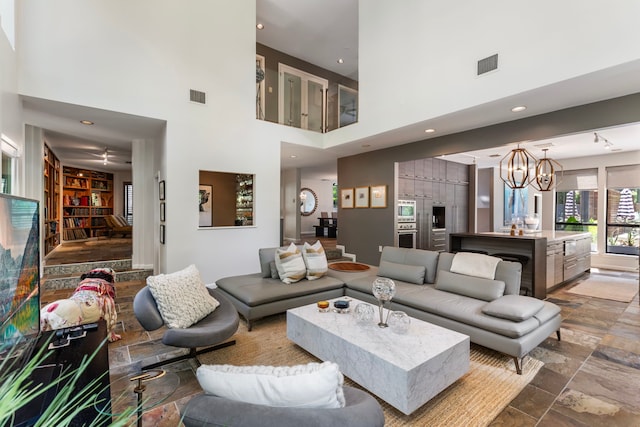 tiled living room with ceiling fan with notable chandelier and a towering ceiling