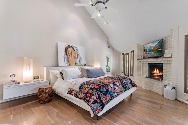 bedroom with ceiling fan, brick wall, light hardwood / wood-style flooring, and high vaulted ceiling