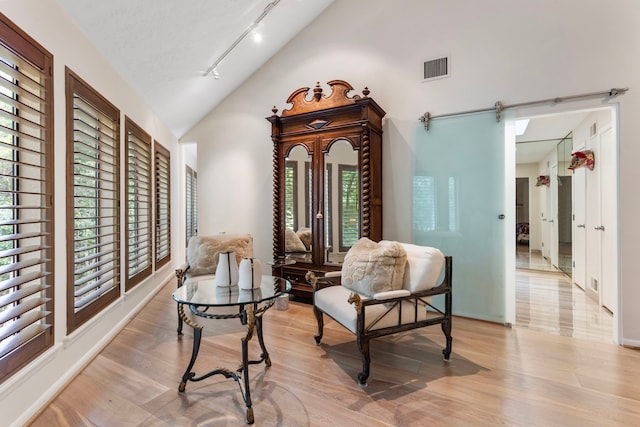 living area with light hardwood / wood-style floors, rail lighting, a barn door, and high vaulted ceiling