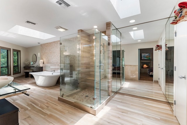 bathroom with a skylight, wood-type flooring, independent shower and bath, and a large fireplace