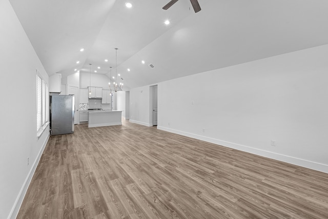 unfurnished living room featuring light hardwood / wood-style floors, ceiling fan with notable chandelier, and vaulted ceiling