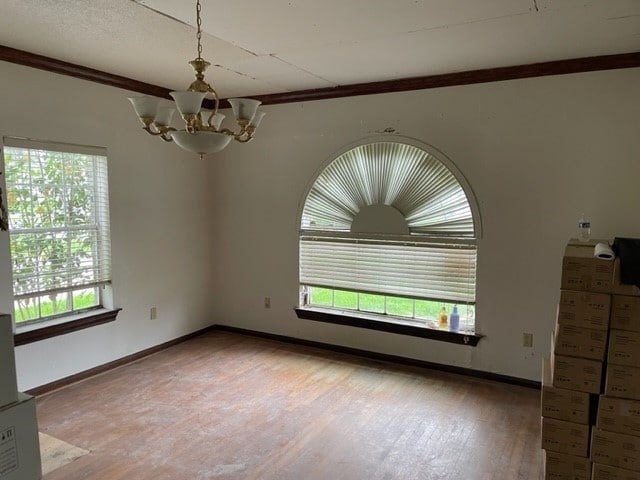 unfurnished room with an inviting chandelier, ornamental molding, hardwood / wood-style flooring, and a wealth of natural light