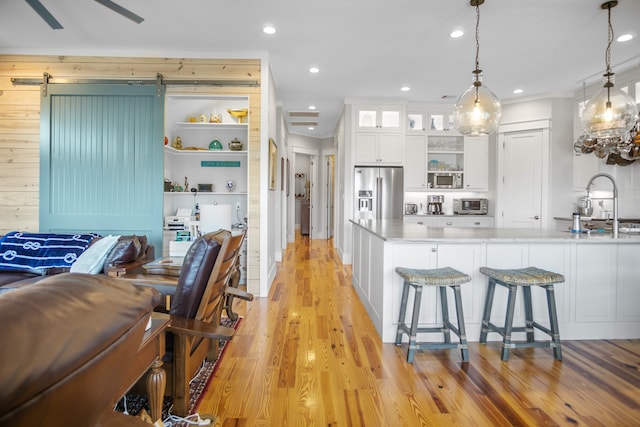 kitchen with stainless steel appliances, a barn door, decorative light fixtures, white cabinetry, and light hardwood / wood-style floors