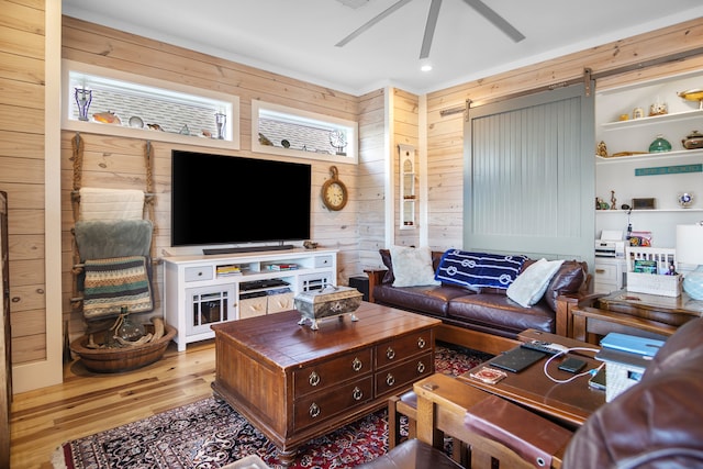 living room with light hardwood / wood-style floors, wood walls, a barn door, and ceiling fan