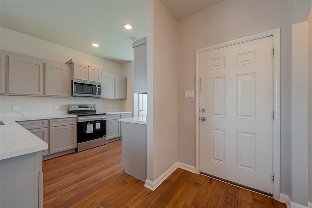 kitchen with light stone countertops, gray cabinetry, stainless steel appliances, and wood-type flooring