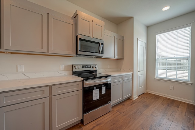 kitchen with light stone counters, gray cabinets, stainless steel appliances, and light hardwood / wood-style floors