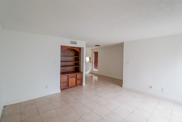 empty room featuring built in features, a textured ceiling, and light tile patterned floors