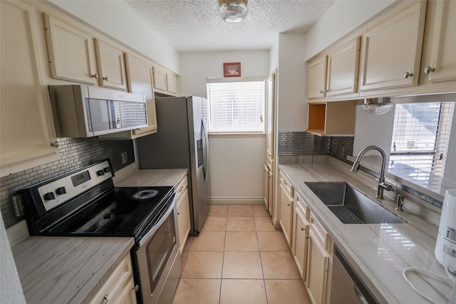 kitchen with light tile patterned floors, a textured ceiling, backsplash, stainless steel appliances, and sink