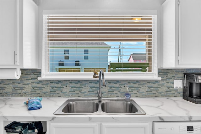 kitchen featuring light stone countertops, sink, white cabinets, and backsplash