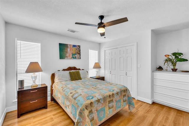 bedroom with a textured ceiling, light hardwood / wood-style flooring, a closet, and ceiling fan