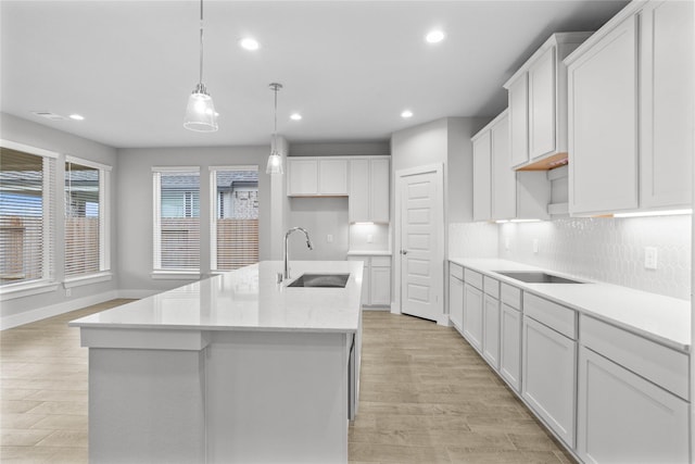 kitchen with sink, white cabinetry, a center island with sink, black electric cooktop, and pendant lighting