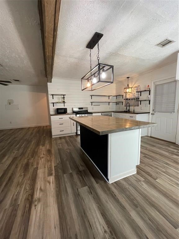 kitchen with white cabinets, stainless steel stove, a kitchen island, a textured ceiling, and dark hardwood / wood-style flooring