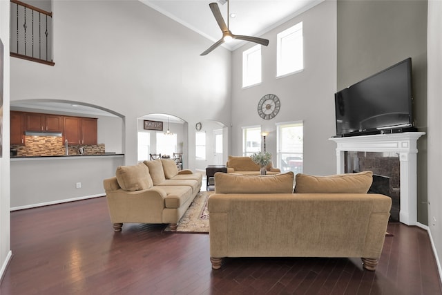 living room featuring a premium fireplace, dark wood-type flooring, ceiling fan, and a towering ceiling