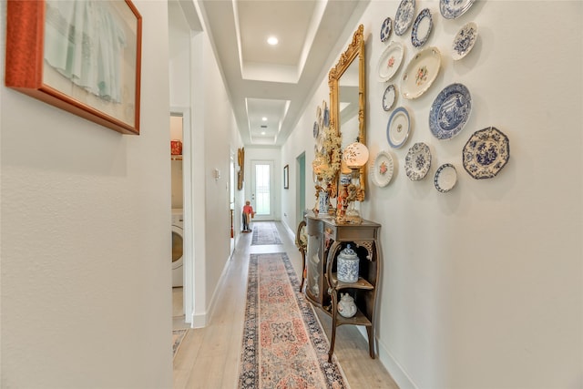 hall featuring light hardwood / wood-style flooring, a tray ceiling, and washer / dryer