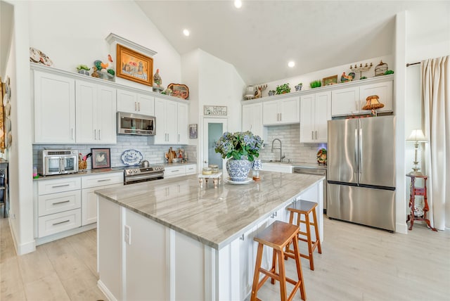 kitchen featuring light wood-type flooring, light stone countertops, a center island, white cabinets, and appliances with stainless steel finishes