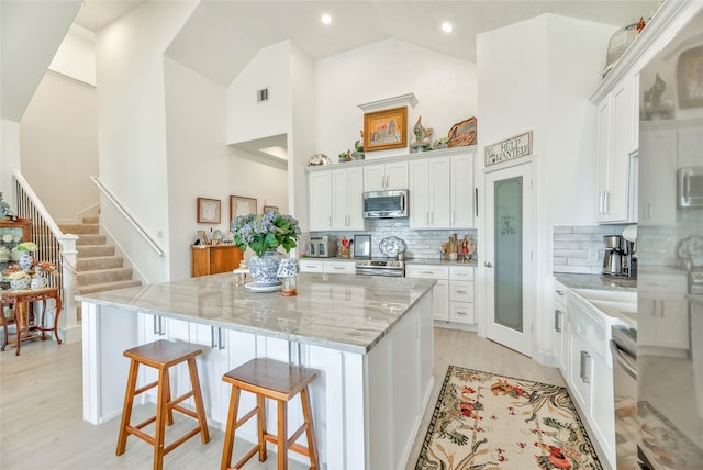 kitchen with appliances with stainless steel finishes, a center island, high vaulted ceiling, and white cabinetry