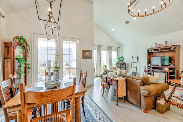 dining area with high vaulted ceiling, an inviting chandelier, and light wood-type flooring