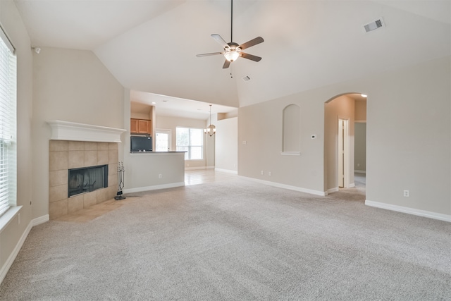 unfurnished living room featuring high vaulted ceiling, a tiled fireplace, ceiling fan with notable chandelier, and light carpet