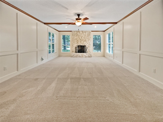 unfurnished living room with ceiling fan, a stone fireplace, crown molding, and a textured ceiling