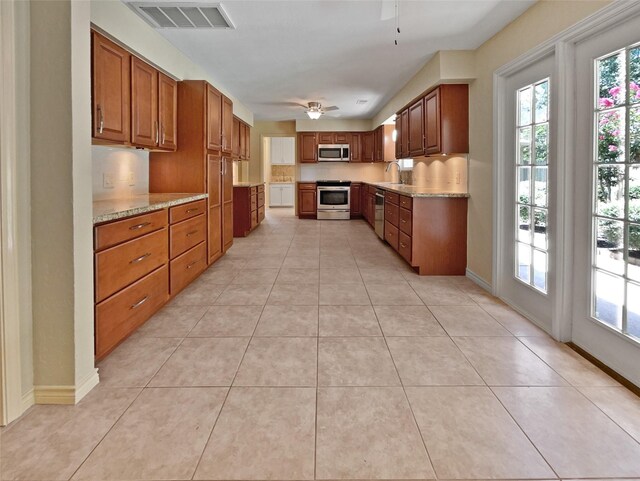 kitchen with stainless steel appliances, sink, light stone counters, light tile patterned floors, and ceiling fan