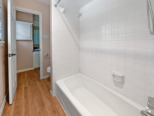 bathroom with hardwood / wood-style flooring, toilet, and tiled shower / bath combo