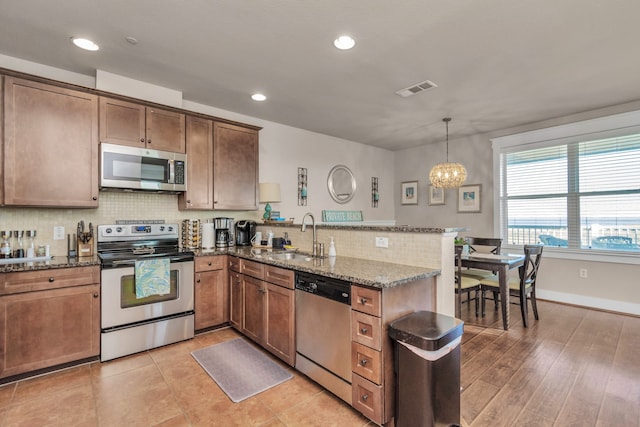 kitchen with dark stone countertops, kitchen peninsula, hanging light fixtures, appliances with stainless steel finishes, and sink