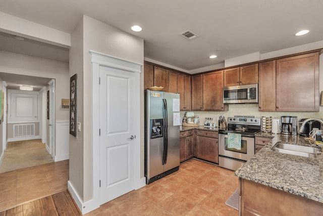 kitchen with light tile patterned flooring, stainless steel appliances, sink, dark stone countertops, and backsplash