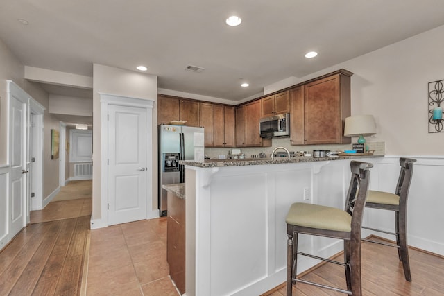 kitchen with light hardwood / wood-style flooring, kitchen peninsula, stainless steel appliances, light stone countertops, and a kitchen breakfast bar