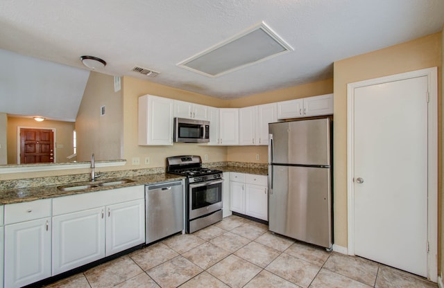 kitchen with dark stone countertops, white cabinets, stainless steel appliances, and sink