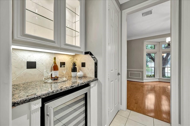 bar featuring light tile patterned flooring, ornamental molding, stone counters, beverage cooler, and decorative backsplash