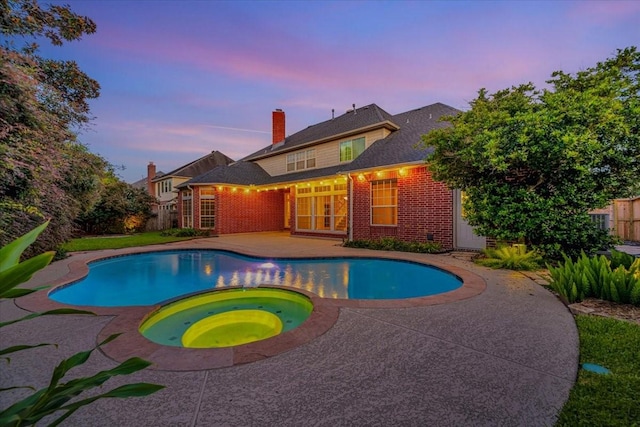 pool at dusk featuring a patio area and an in ground hot tub