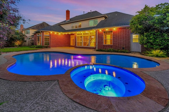 pool at dusk featuring a patio area and an in ground hot tub