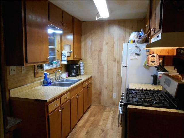 kitchen featuring range with gas cooktop, wooden walls, sink, and light wood-type flooring