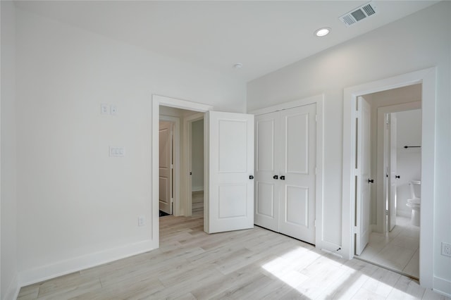 unfurnished bedroom with ensuite bathroom and light hardwood / wood-style flooring